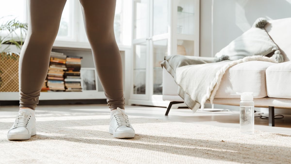 A woman in activewear preparing for an indoor workout with a bottle of water nearby.